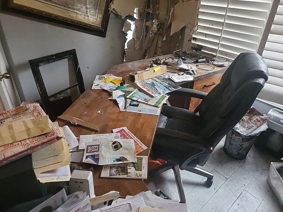 Fire and smoke damaged home office with debris covering desk and floor